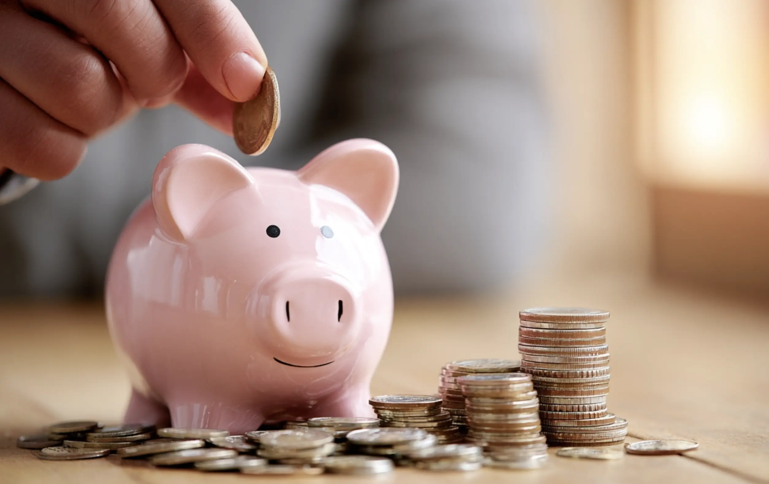 Hand putting coin into pink piggy bank representing affordable life insurance savings and financial planning