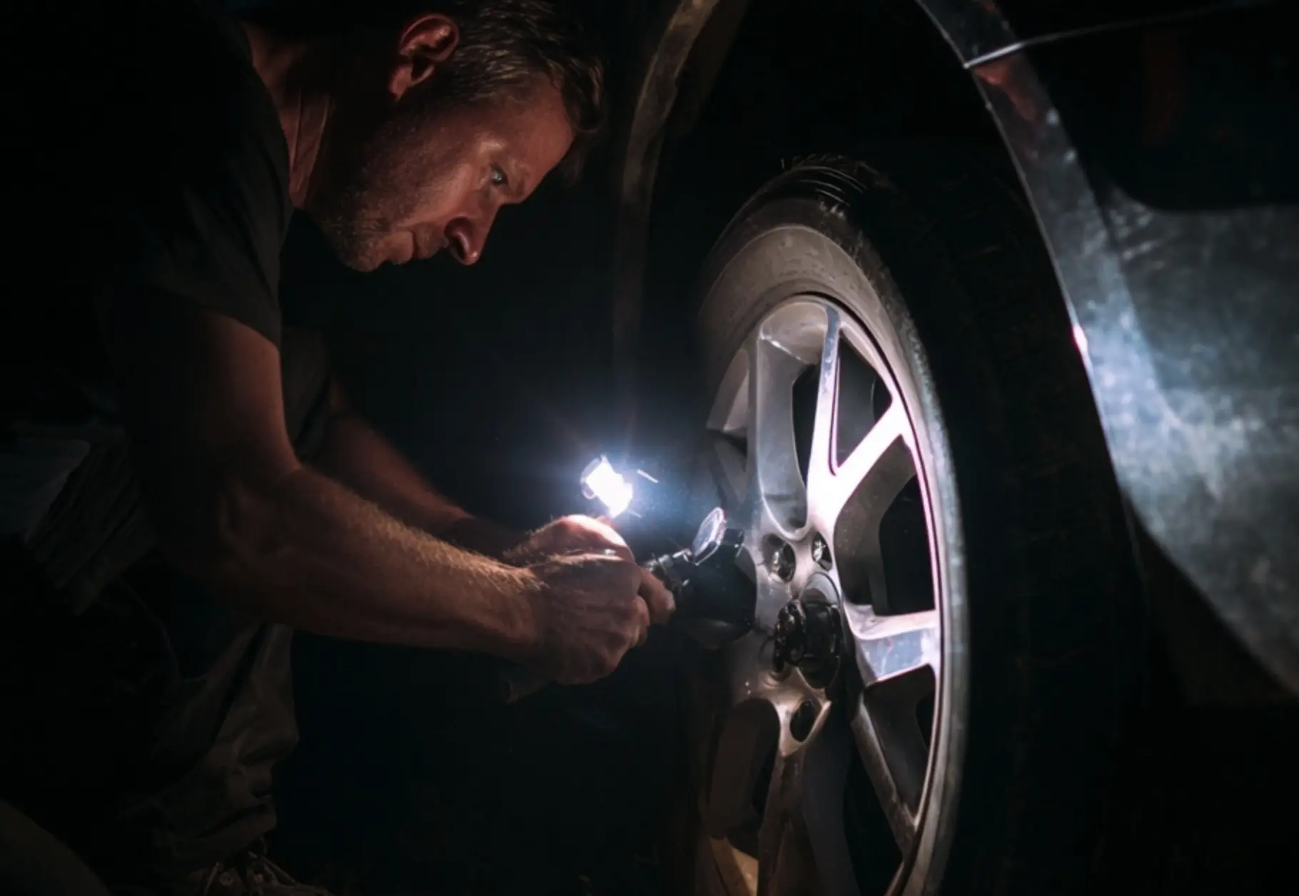 Emergency nighttime car wheel repair with flashlight - UK breakdown cover 24/7 roadside assistance