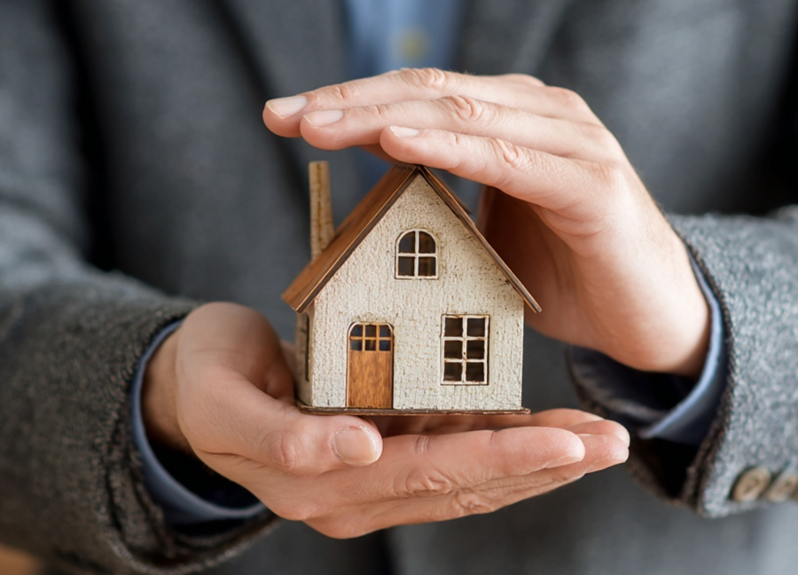 Hands protecting miniature house model representing buildings insurance coverage