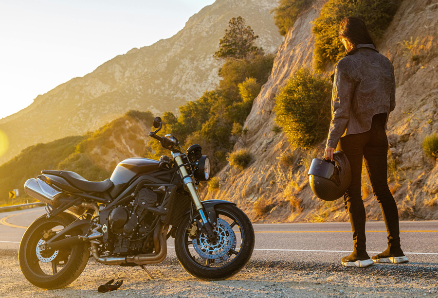 Motorcyclist with helmet standing next to modern sport bike on scenic mountain road during golden hour